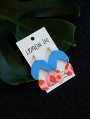 Pair of blue and pink earrings on a branded card with green leaves in the background