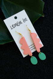 Pair of coral and green earrings on a branded card with a dark background.