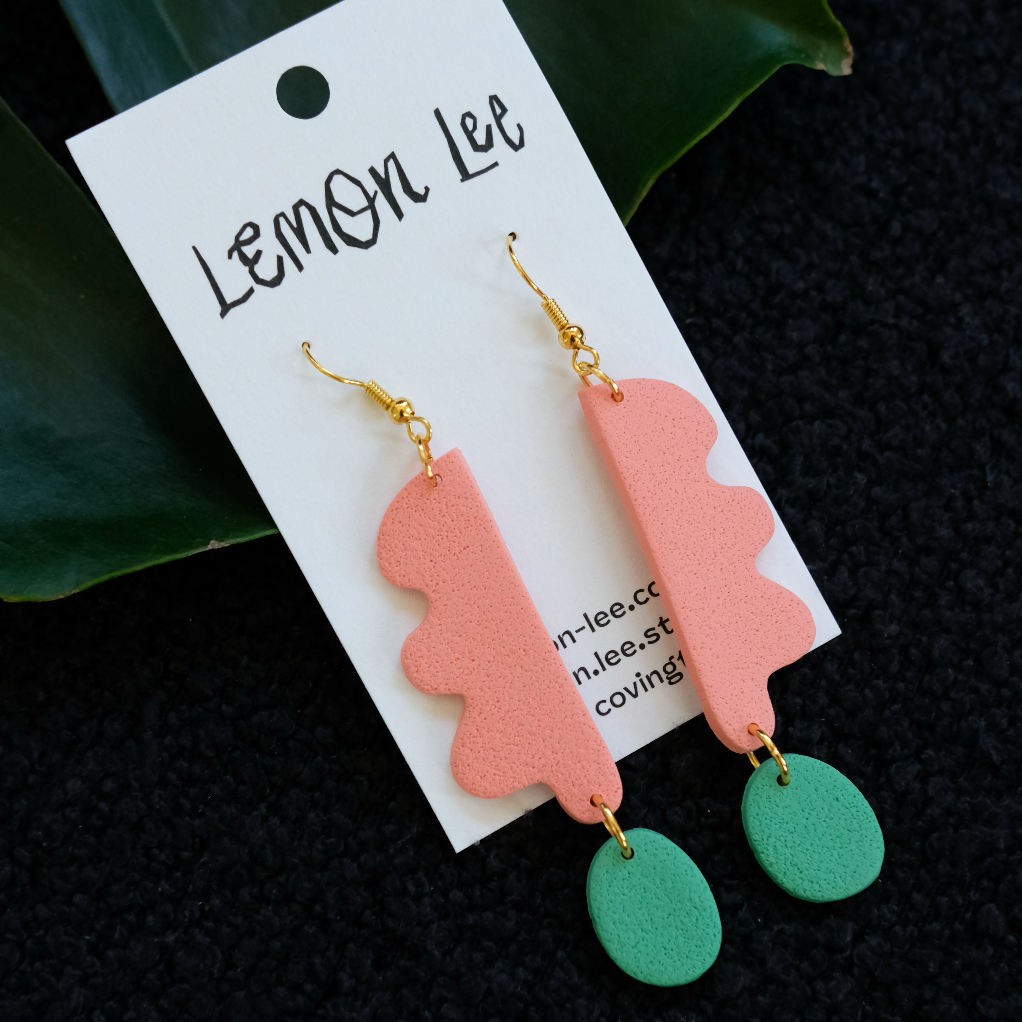 Pair of coral and green earrings on a branded card with a dark background.
