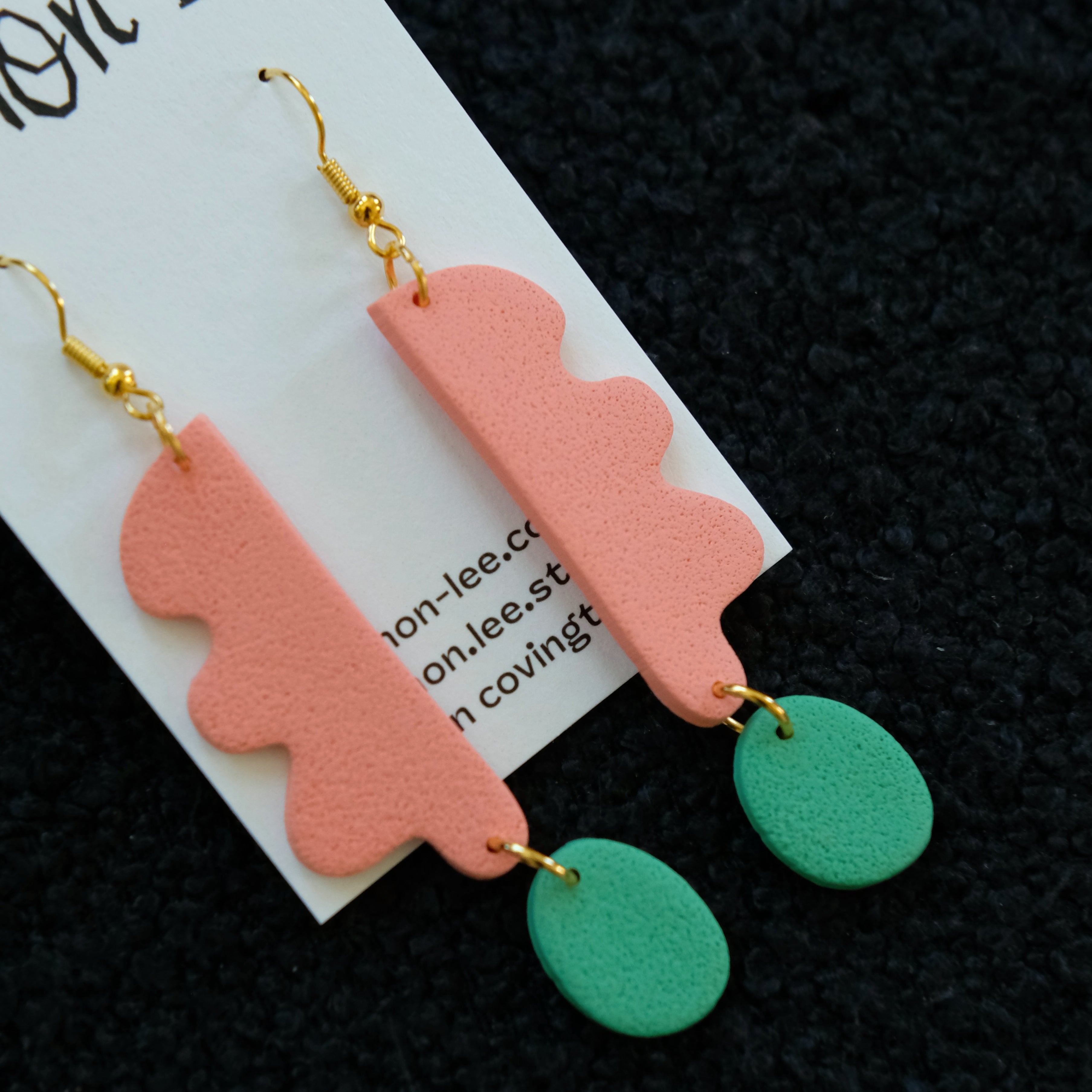 Pair of coral and green earrings on a dark background.