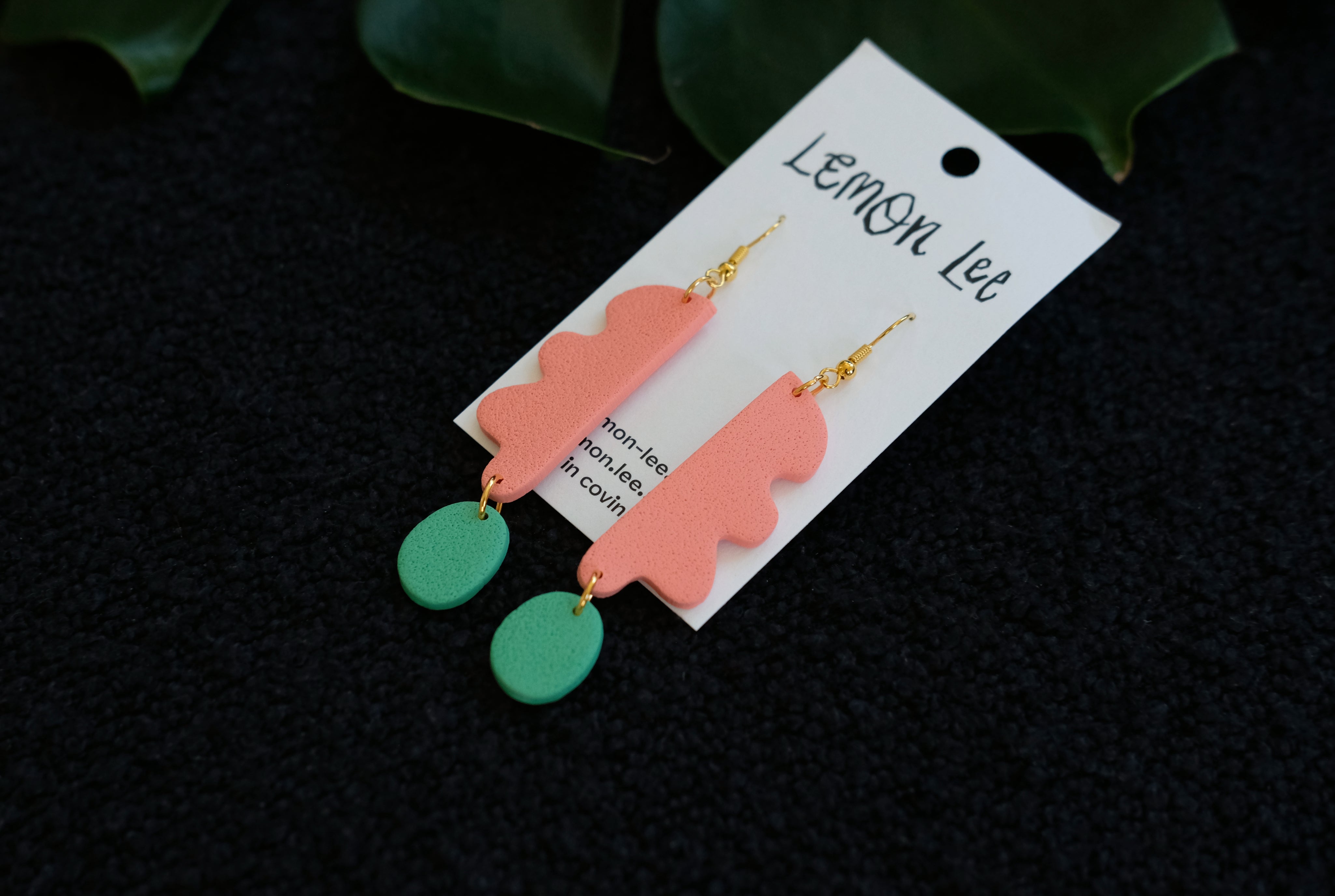 Pair of coral and green earrings on a branded card against a dark background.