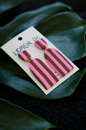 Pink and brown striped earrings on a branded card with green leaves in the background