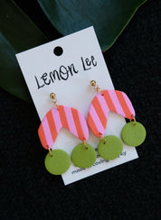 Colorful Pink and Green striped earrings on a branded card against a dark background