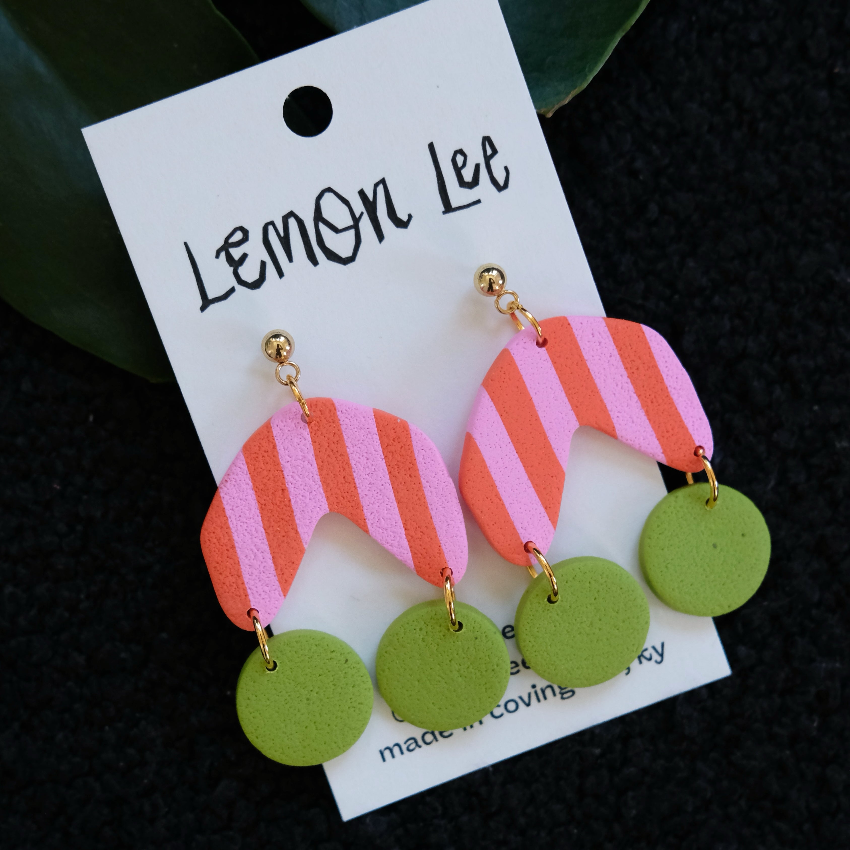 Colorful Pink and Green striped earrings on a branded card against a dark background