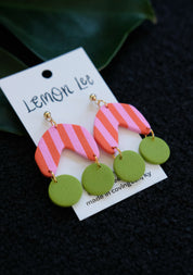 Colorful Pink and Green striped earrings on a branded card against a dark background
