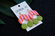 Colorful Pink and Green striped earrings on a branded card against a dark background