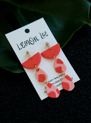 Red and pink earrings on a branded card against a dark background