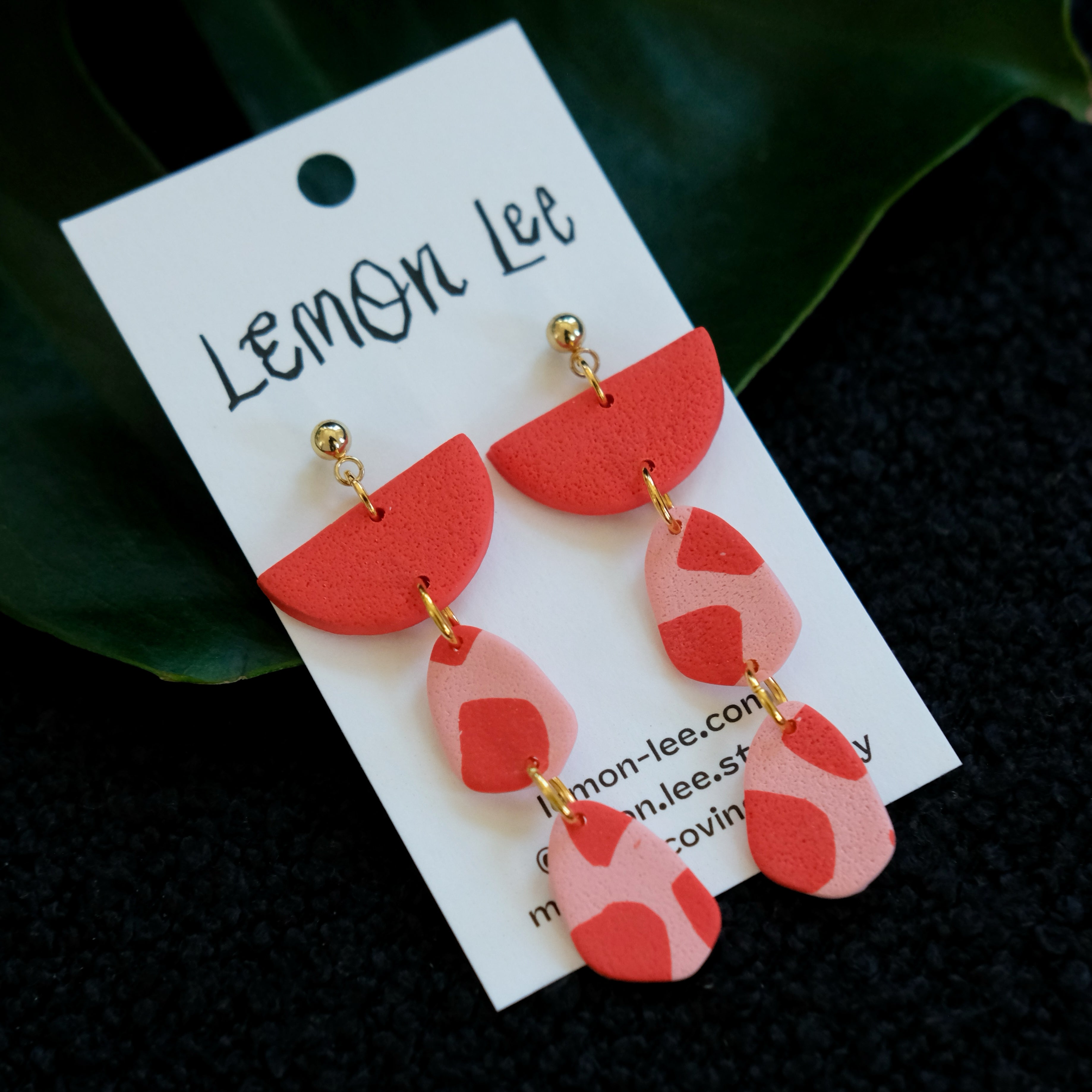 Red and pink earrings on a branded card against a dark background